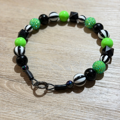 A beaded stretch bracelet featuring black, white, and neon green beads, displayed on a light wood grain surface.