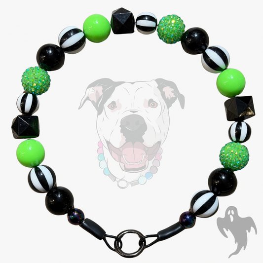 A beaded dog collar featuring black and white striped beads, solid bright green beads, glittery green beads, and black faceted geometric beads, displayed against a light gray background with a faint dog graphic.