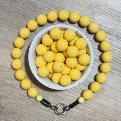 Yellow beaded bracelet arranged in a circle around a small white bowl filled with matching yellow beads, on a light wood surface.
