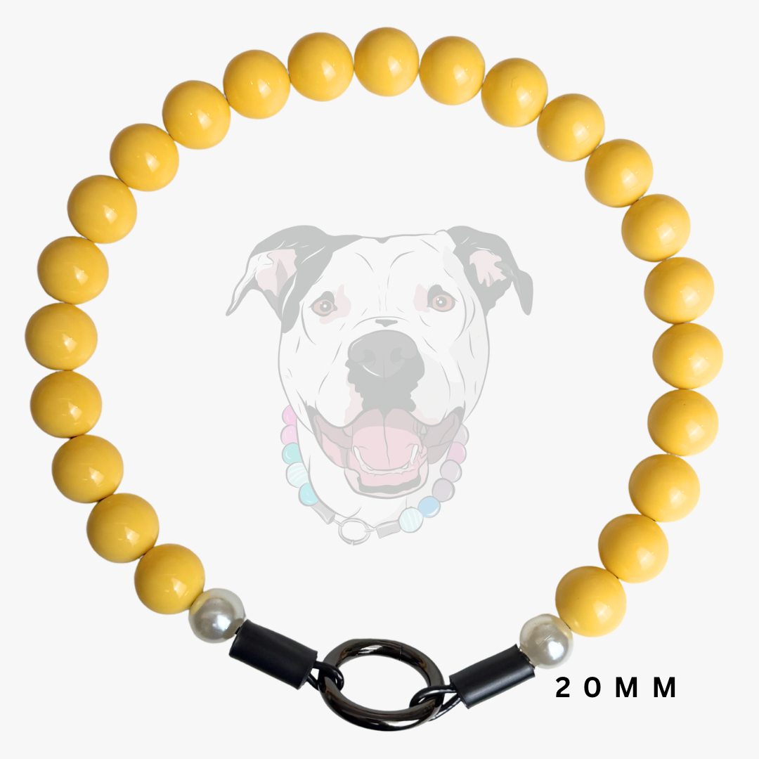 A yellow beaded dog collar with glossy round beads, a black metal ring clasp, and two small white pearl-like accent beads. A faint graphic of a dog wearing the collar is shown behind it on a light gray background, with '20 MM' text at the bottom right.