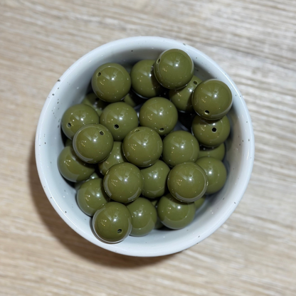 Olive green acrylic 20mm beads with pre-drilled holes, displayed in a small speckled white ceramic bowl on a light wood grain surface.