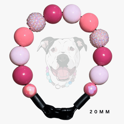 A pink beaded dog collar with alternating smooth round beads and two textured, sparkly iridescent beads, featuring a black plastic clasp. A faint graphic of a dog wearing the collar is visible in the background, with '20MM' text in the bottom right corner.