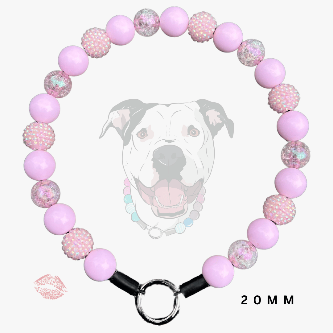 A pink beaded dog collar with alternating smooth light pink beads and textured pink-and-white speckled beads, featuring a silver metal ring clasp and black connector ends. A faint dog face graphic appears behind the collar, with a small lip print and '20MM' text on a light gray background.