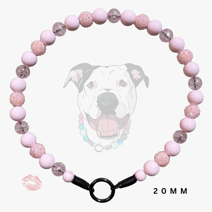 A pink beaded collar with alternating smooth light pink beads and glittery pink beads, featuring a black metal ring clasp. A faint dog graphic and a lip print are visible in the background, with '20MM' text at the bottom right.