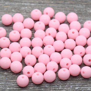 A pile of small, round, light pink beads with holes, arranged on a gray wood-textured surface.
