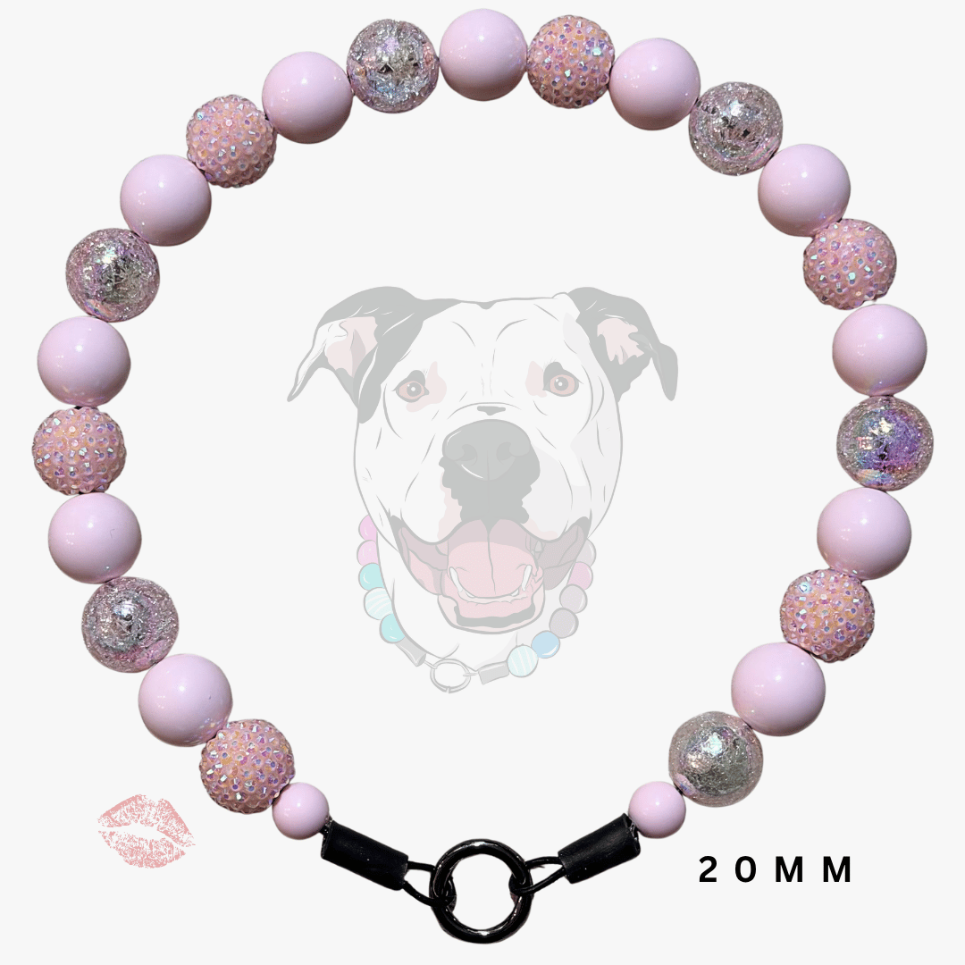 A pink beaded dog collar with light pink matte beads, glittery pink beads, and silver glitter accent beads, featuring a black metal ring clasp. A faint graphic of a dog's face is in the background, with a small lip print and '20MM' text overlay.