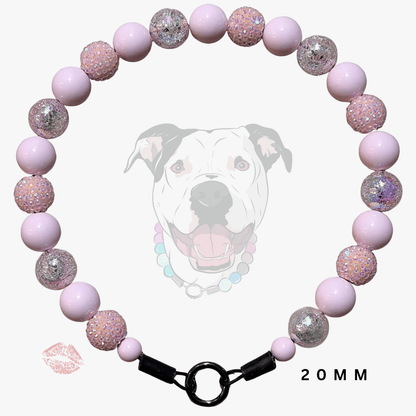 A pink beaded dog collar with light pink matte beads, glittery pink beads, and silver glitter accent beads, featuring a black metal ring clasp. A faint graphic of a dog's face is in the background, with a small lip print and '20MM' text overlay.