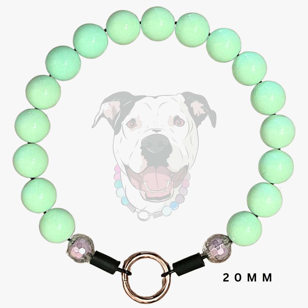 A beaded dog collar featuring light mint green round beads, a rose gold metal split ring, and black toggle closures with faceted purple beads. A faint graphic of a dog wearing the collar is displayed in the background, with '20MM' text on the bottom right.