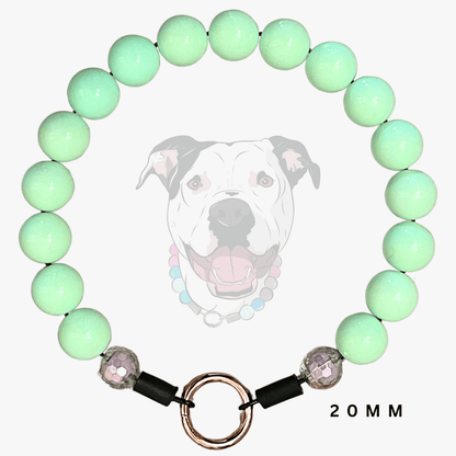 A beaded dog collar featuring light mint green round beads, a rose gold metal split ring, and black toggle closures with faceted purple beads. A faint graphic of a dog wearing the collar is displayed in the background, with '20MM' text on the bottom right.