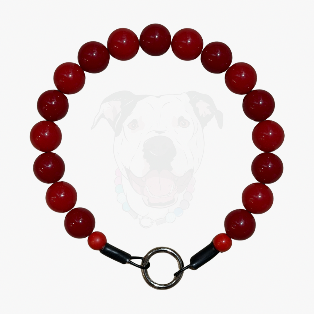 A red beaded dog collar with a metal ring clasp and black accents, displayed against a light gray background with a faint dog graphic.