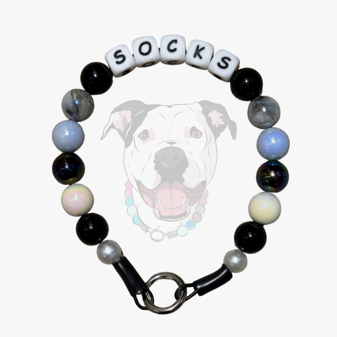 Custom Beaded Pet Collar Laying Flat on a White background, the collar features alternating black, white, grey and marbled black 16mm A.B Beads on aircraft grade stainless steel wire and 12mm silicone letter beads that say SOCKS from POPNCO beaded pet collars. 
