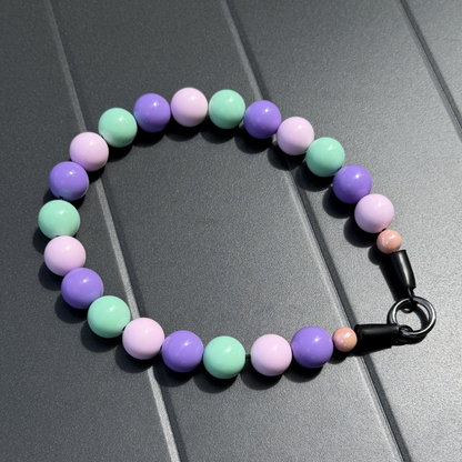 Pink, Purple, and Teal green popnco beaded pet collar named Stacey with a black o ring on a gray surface
