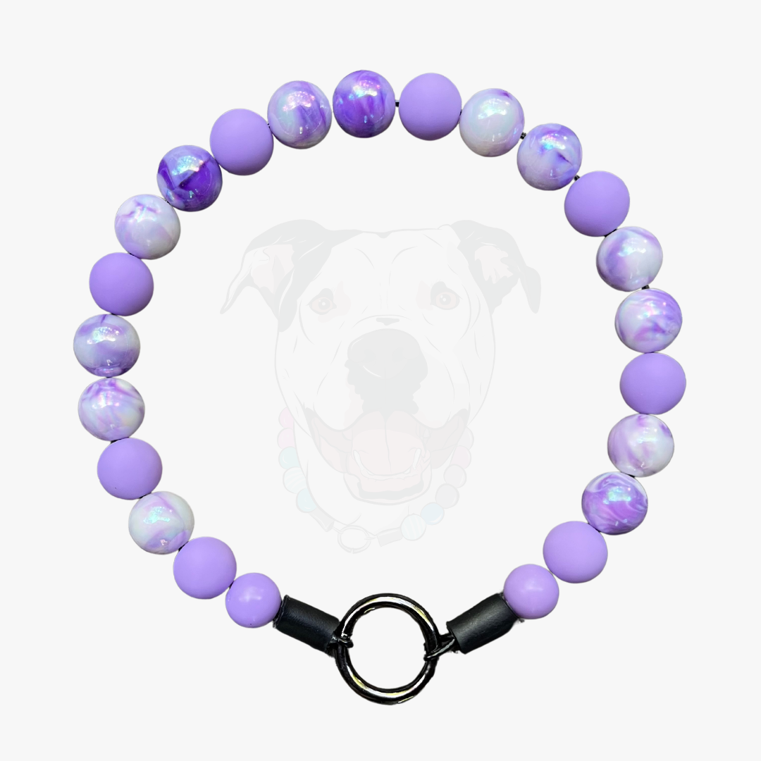 A beaded dog collar featuring light purple and white marbled beads, secured with a black metal ring clasp, shown against a light gray background with a faint dog graphic.