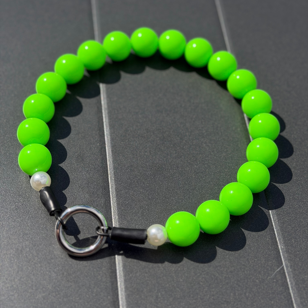 Green beaded pet collar called Viper laying flat on a gray surface