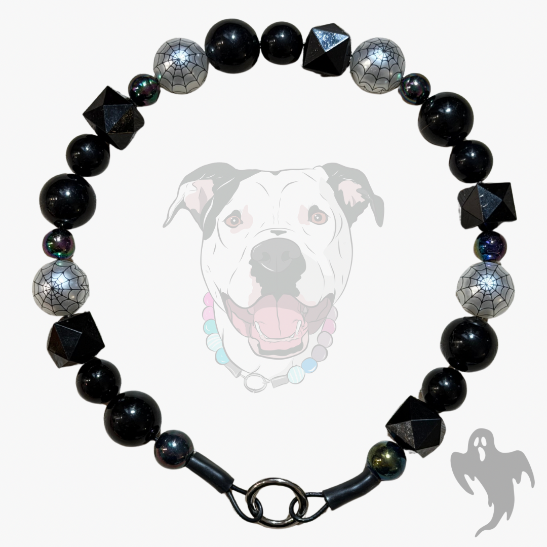 A beaded dog collar featuring glossy black round beads, spiderweb-patterned silver beads, and faceted black geometric beads, displayed against a light gray background with a faint dog graphic.