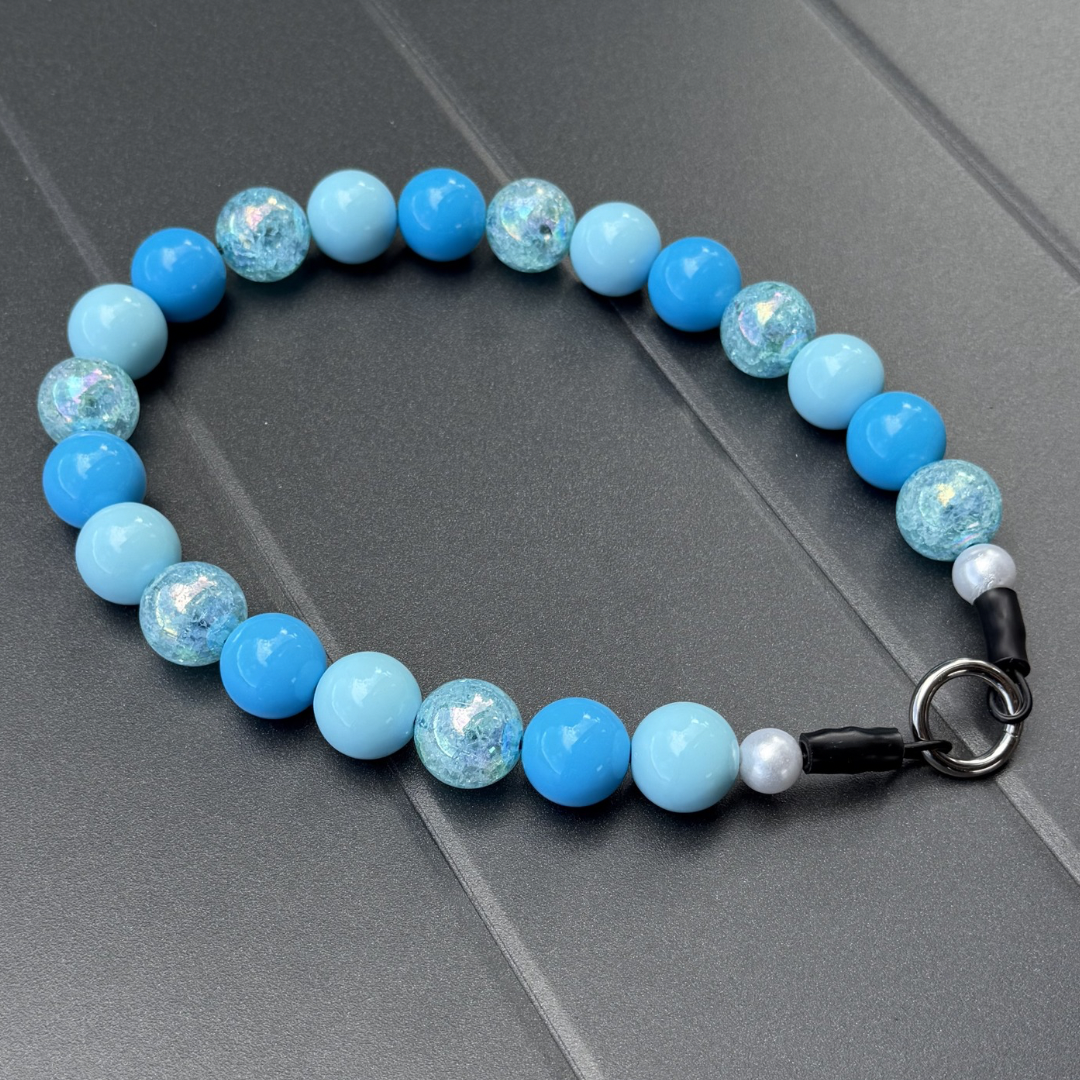 POPNCO Abominable Snowman Winter Holiday Collection Beaded Pet Collar. Blue acrylic and resin beads on aircraft grade stainless steel wire.on a Grey Table Top.
