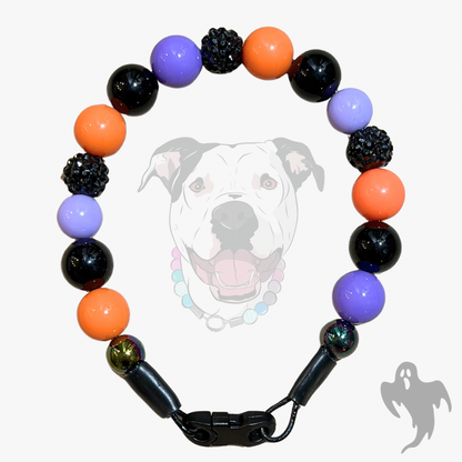 A beaded dog collar with alternating orange, purple, and black beads, including textured black spacers, shown against a light gray background with a faint dog graphic.