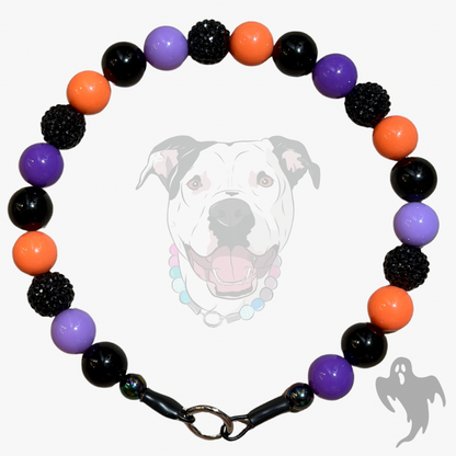 A beaded dog collar with alternating black, purple, and orange beads, featuring textured black spiky beads, a black clasp, and a white dog graphic in the background.