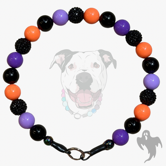 A beaded dog collar with alternating black, purple, and orange beads, featuring textured black spiky beads, a black clasp, and a white dog graphic in the background.