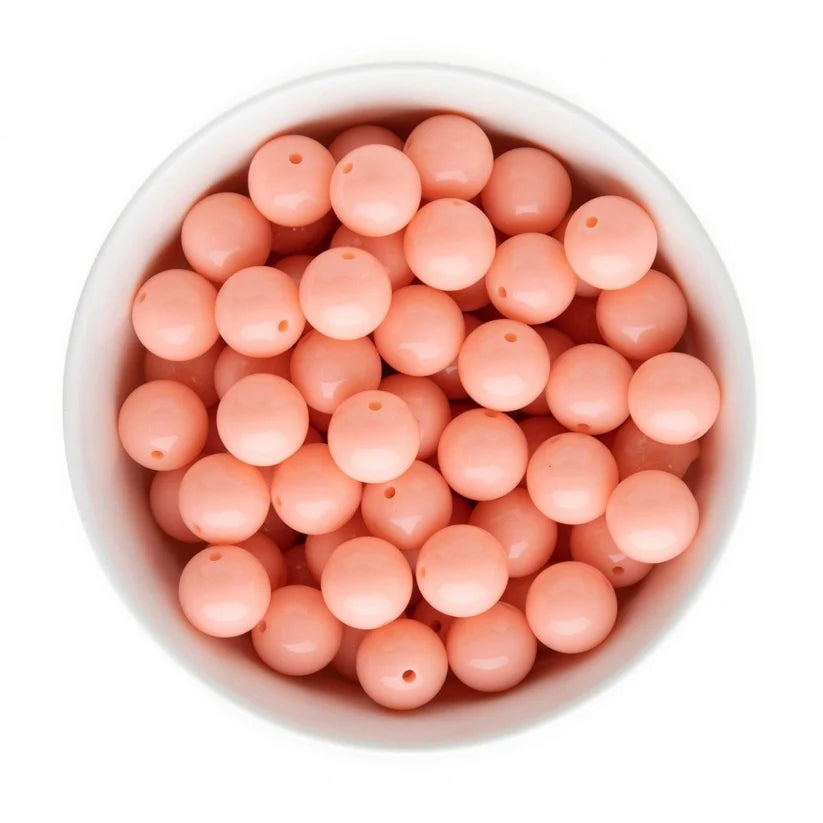 Top-down view of round peach-pink beads with holes, arranged inside a white bowl on a white background.