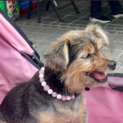 Dog wearing a pink beaded necklace in a pink stroller with text about a handmade necklace from @poppnco.pnp