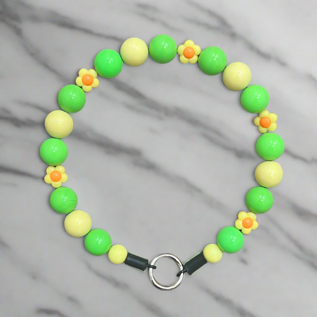 Bracelet with green and yellow beads and flower decorations on a gray background