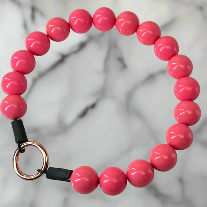 Pink beaded bracelet with a black and rose gold clasp on a marble background
