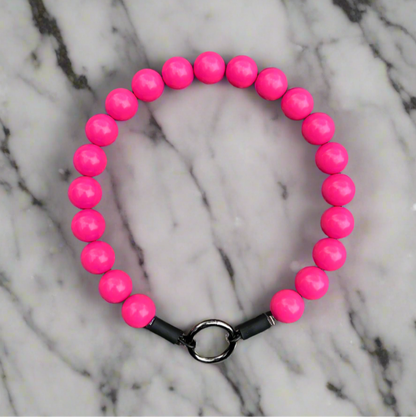 Pink beaded bracelet with a black clasp on a marble background