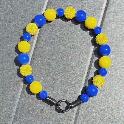 Video of the POPNCO beaded pet collar Homer from the Biggie Smalls collection, featuring alternating Yellow and Blue acrylic beads on aircraft grade stainless steel wire on a grey table. 