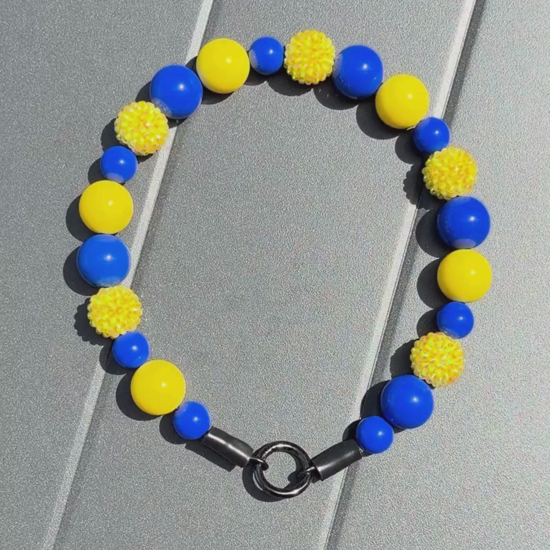 Video of the POPNCO beaded pet collar Homer from the Biggie Smalls collection, featuring alternating Yellow and Blue acrylic beads on aircraft grade stainless steel wire on a grey table. 