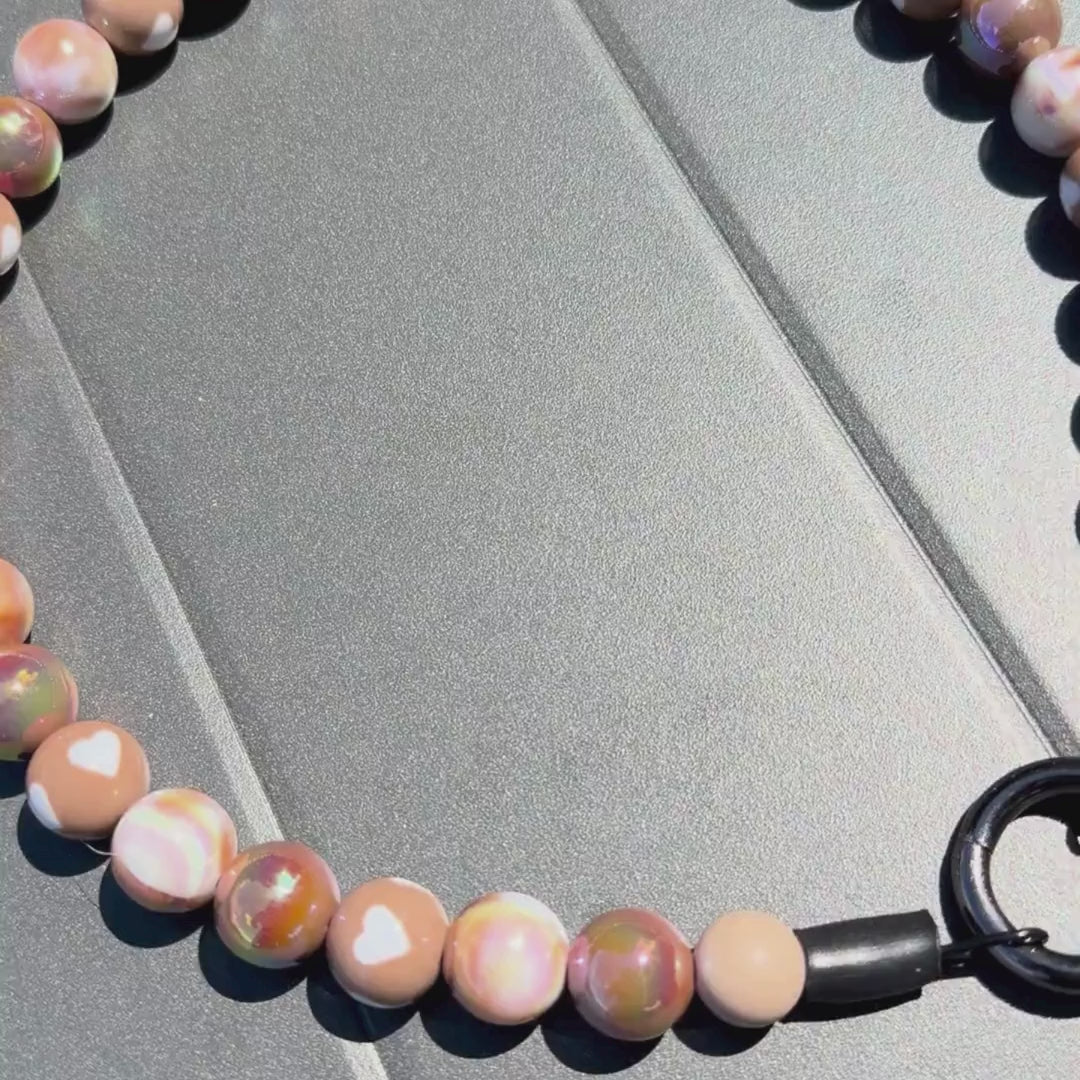 Video of Indulgence POPNCO beaded pet collar. The Beaded Collar is crafted on aircraft grade stainless steel wire and the waterproof beads are AB Shiny iridescent shades of brown in a alternating pattern mixed with double sided brown and cream hearts laying on grey surface.